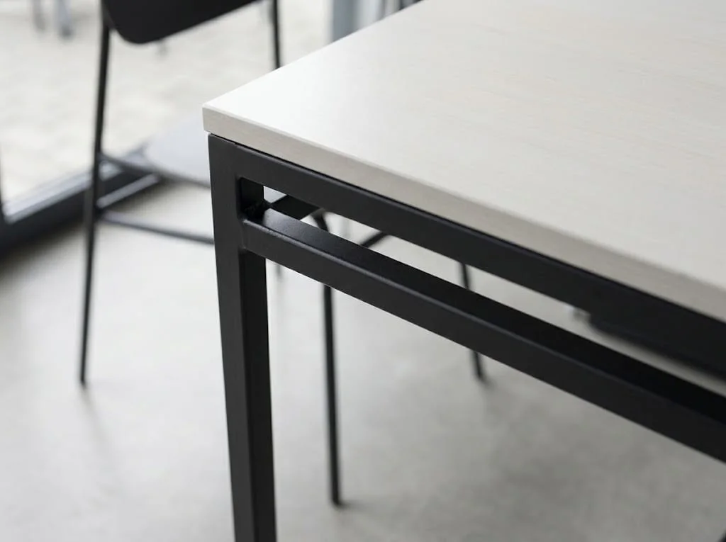 Detail of a metal table with slim legs and a light top.